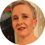 A person with short grey hair, wearing earrings and make-up, is smiling slightly in front of a blurred, colourful background inspired by Ealaín na Gaeltachta.