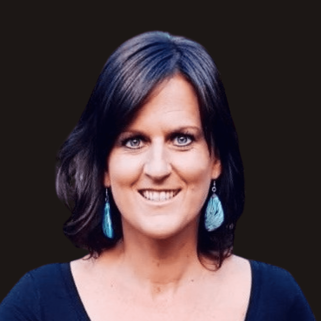 A woman with shoulder-length brown hair, blue earrings, and a black top smiles at the camera against a solid black background, embodying the creative spirit of Ealaín na Gaeltachta.